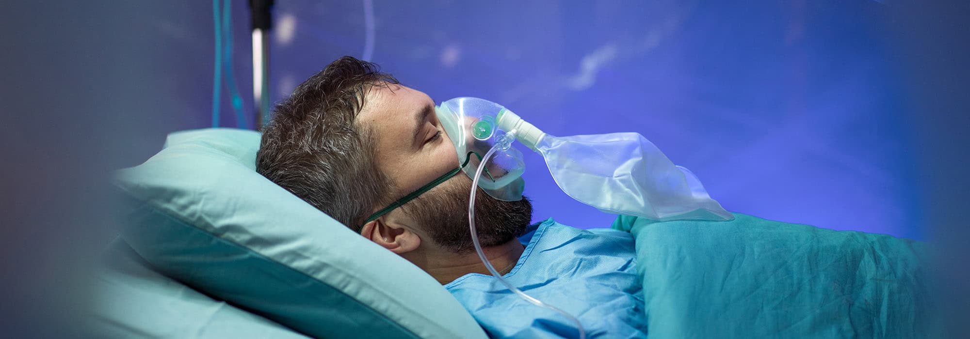 Man with a ventilator mask on in a hospital bed
