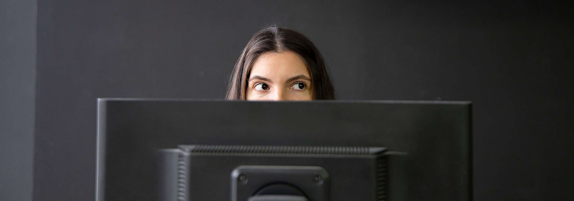 woman peaking over her computer in a dark room