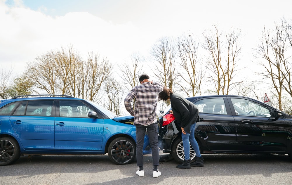 Young male and female drivers looking at damaged car hit